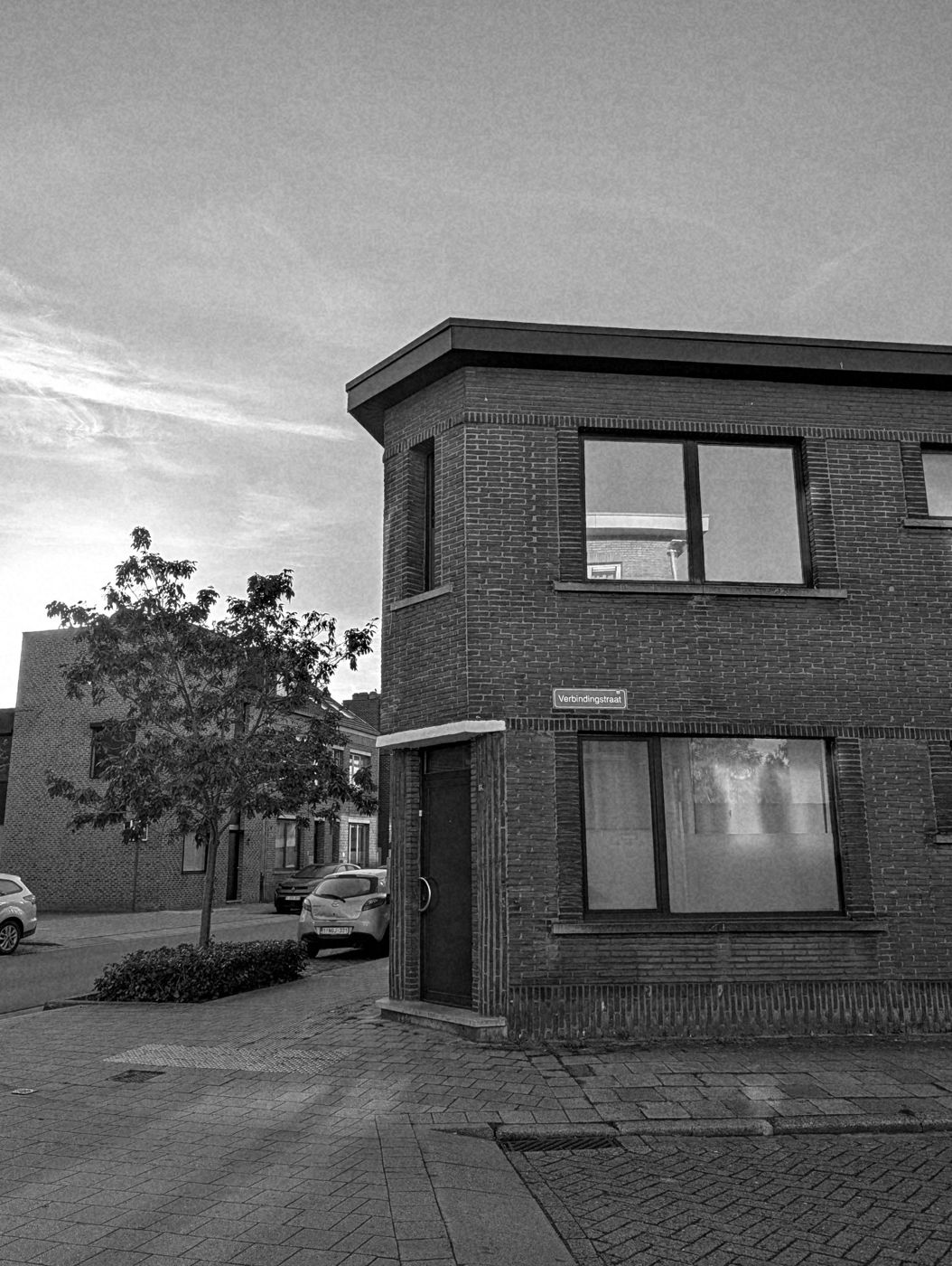 Hoekhuis in baksteen met plat dak en straatnaambord Verbindingstraat, avondlucht en een jonge boom